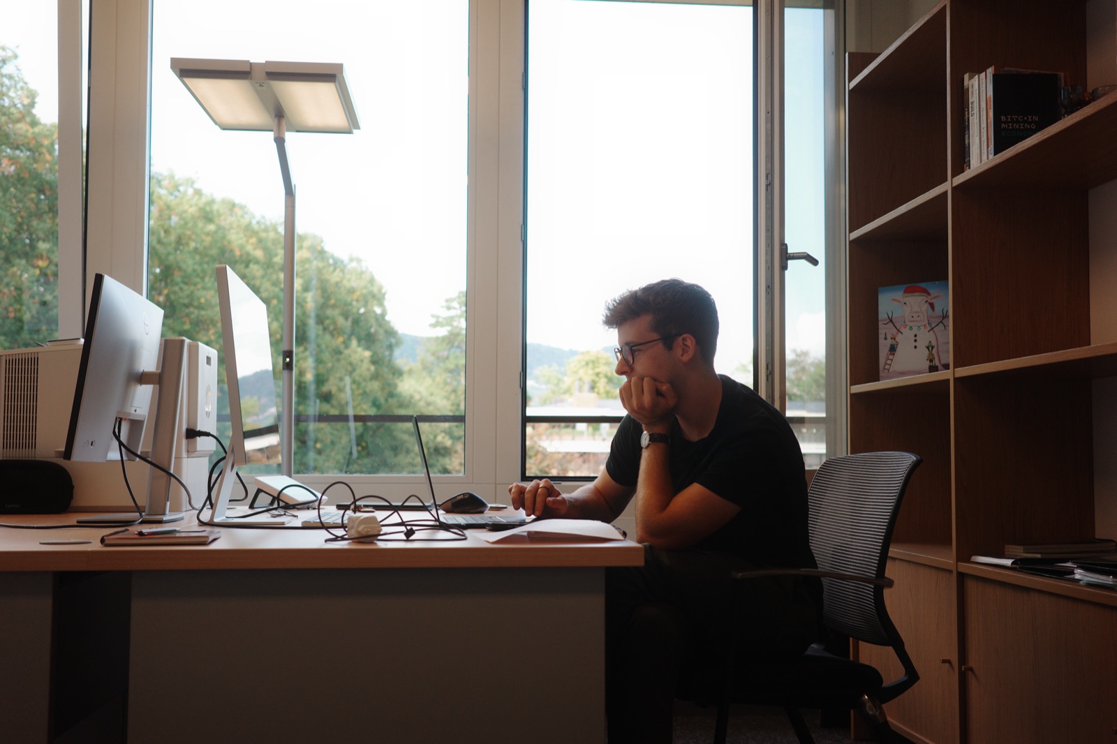 One of us at a desk by the window, thinking.
